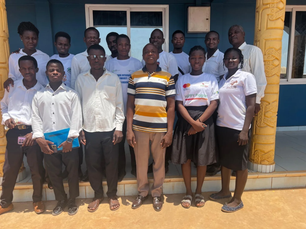 Group photo of missionaries and facilitators from Globeserve Missionary School standing in two rows on a porch in front of a blue-walled building in Northern Ghana, with participants wearing white program t-shirts and casual attire