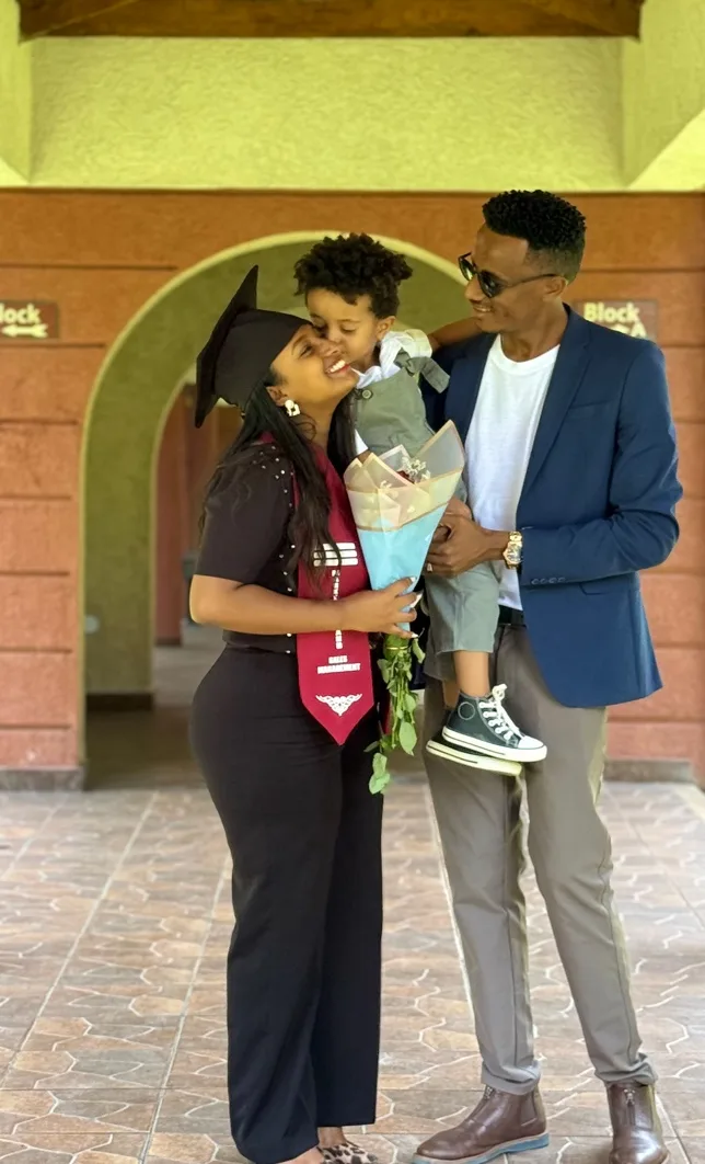 Yanet in her graduation cap and stole kissing her young son, who is held by her husband, beneath an archway on campus