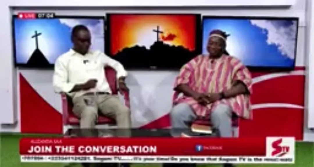 Rev. Samson Abukari and the programme host seated in a television studio, with screens showing crosses behind them and a Join the Conversation banner across the bottom