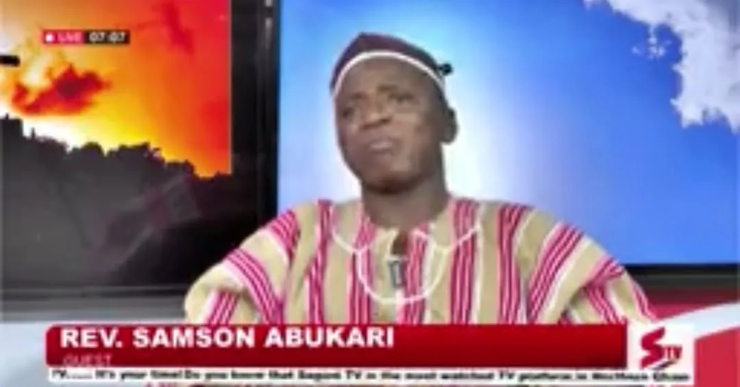 Rev. Samson Abukari speaking as a guest on a live television programme, wearing a striped traditional smock and cap
