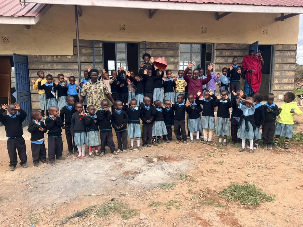 Pupils of Ololepo Hope Comprehensive School in uniform waving with teachers in front of a classroom building