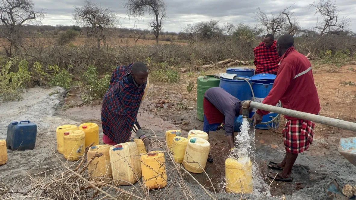 Water gushing from a pipe into a yellow jerrycan as community members fill containers at the borehole