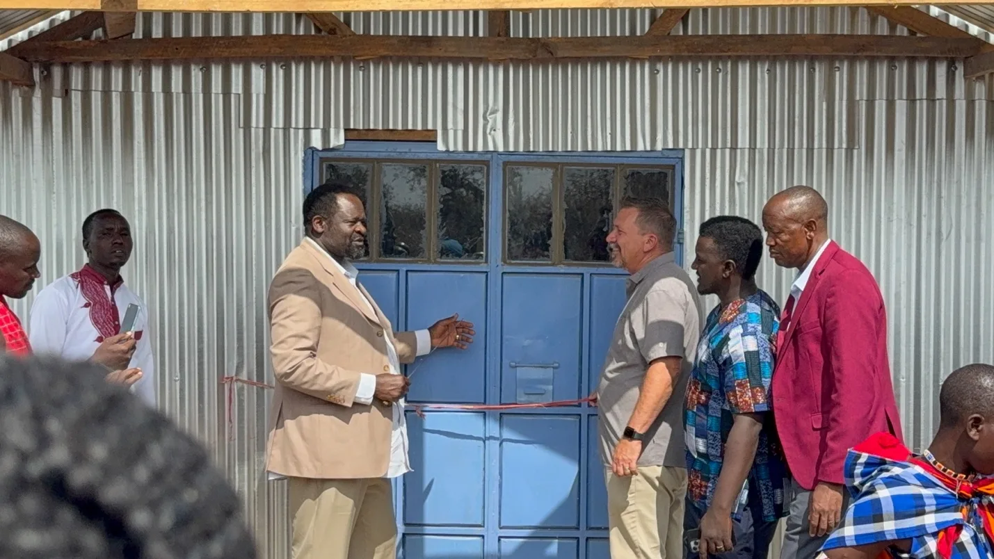 Dr. Okongo and Pastor Randy cutting a red ribbon at the blue doors of the new church, with church leaders standing beside them