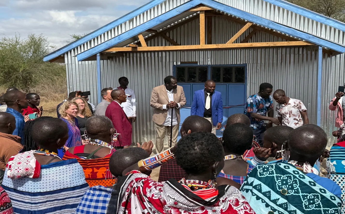 Church leaders standing at the entrance of the newly built corrugated iron church as community members in colourful Maasai shukas gather in front