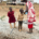 A mother in a red shuka gives water from a bottle to a small boy while a young girl in a red dress stands beside them near the borehole