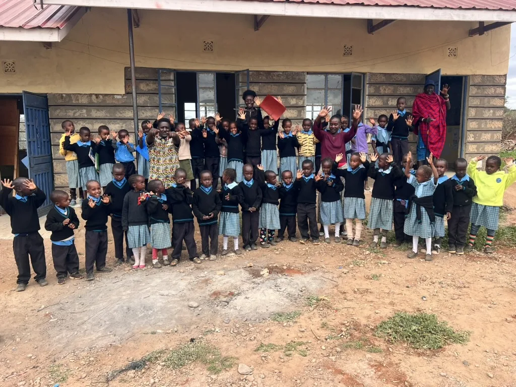 A group of young pupils in black and blue uniforms waving with their teachers outside the school building